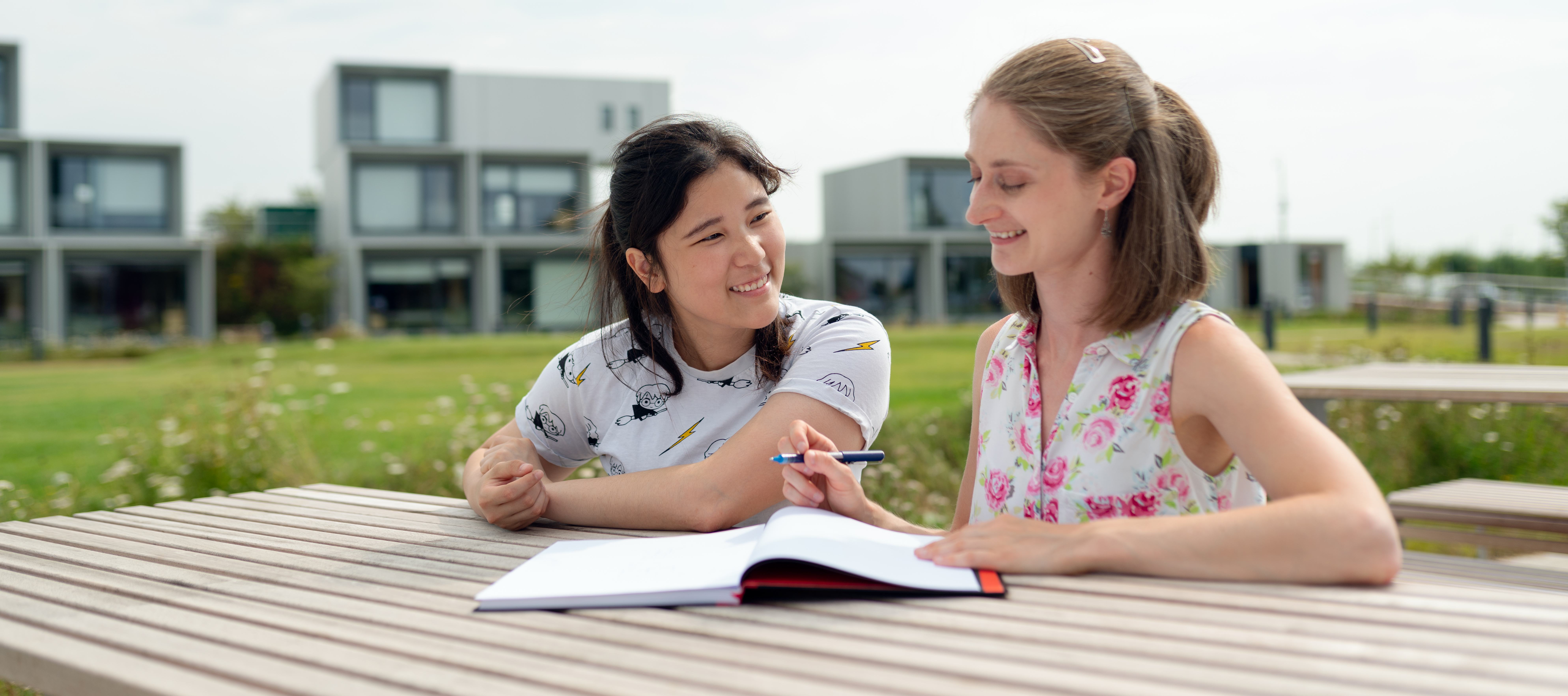 Two people sitting at a table with one helping the other study.